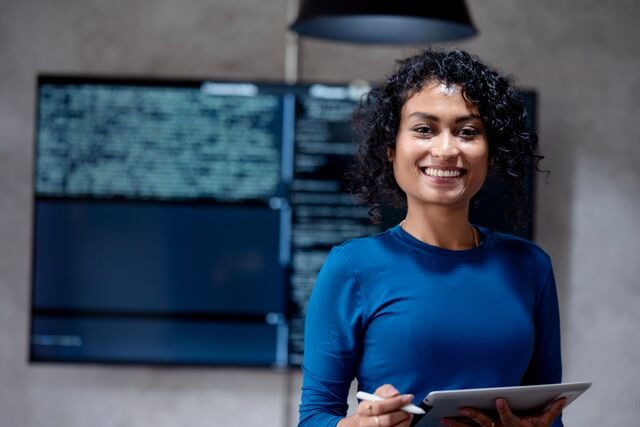 Person holding a tablet in front of a large digital screen displaying data and text, representing modern data analysis and smart technology in a professional setting.